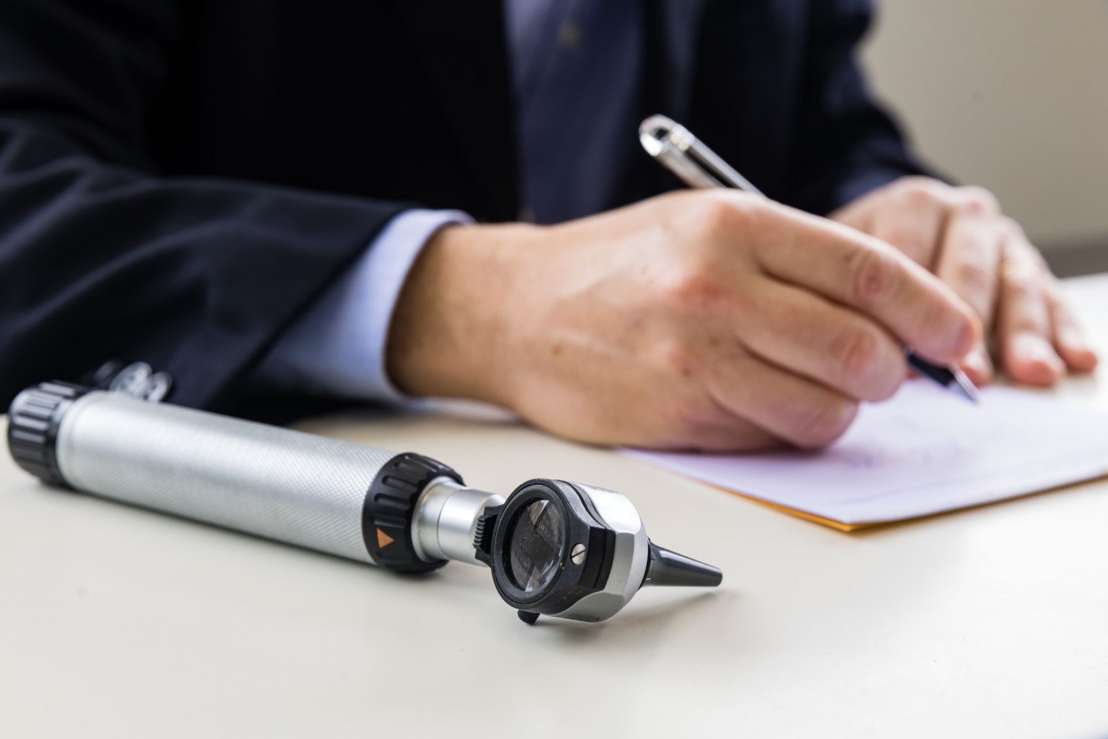 Otoscópio sobre a mesa de consulta enquanto o médico preenche uma receita